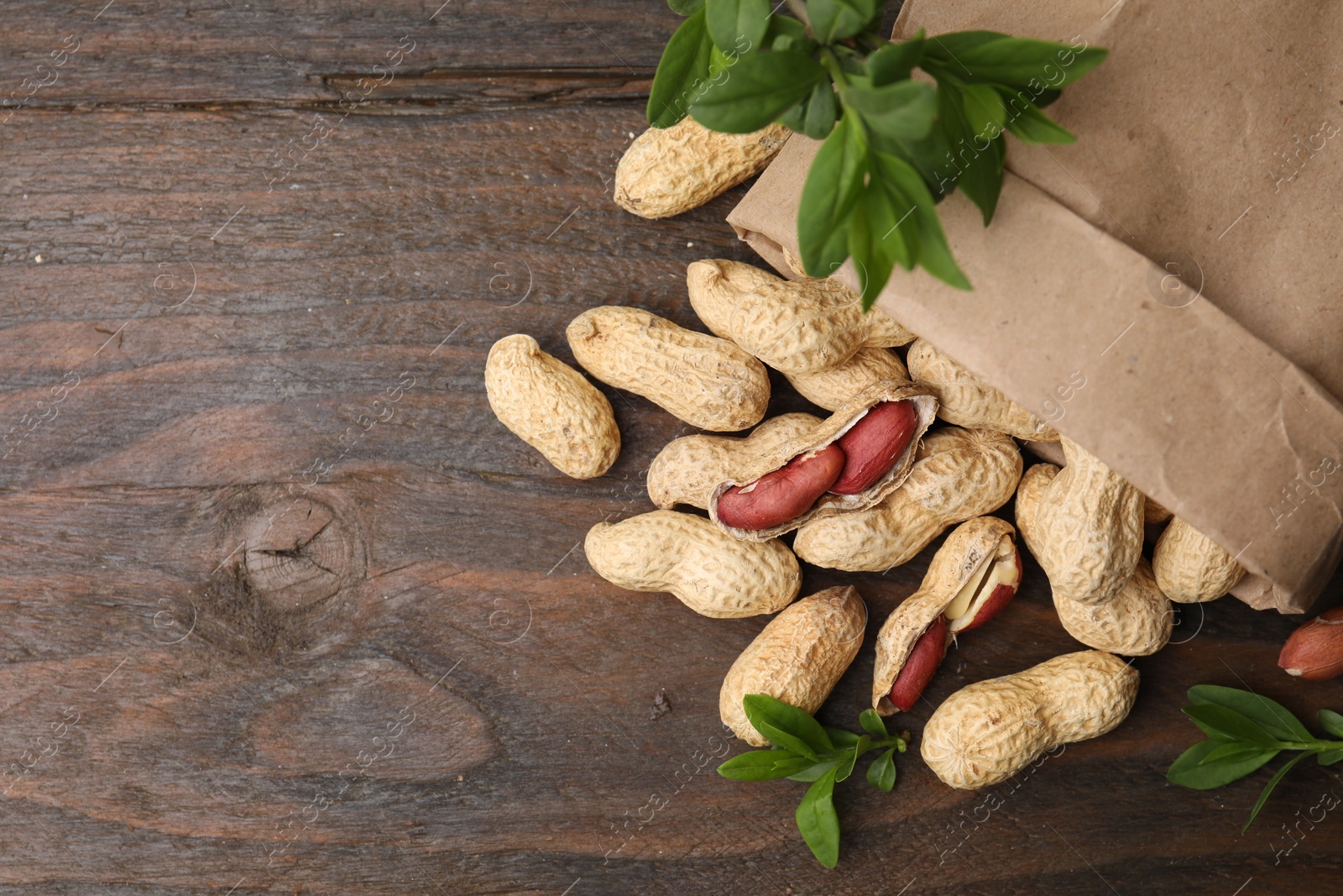 Photo of Paper bag with fresh peanuts and leaves on wooden table, flat lay. Space for text