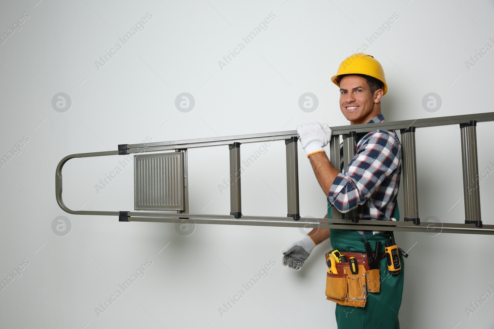 Photo of Professional builder carrying metal ladder on light background