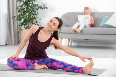 Photo of Woman doing fitness exercises while her daughter sitting on sofa at home