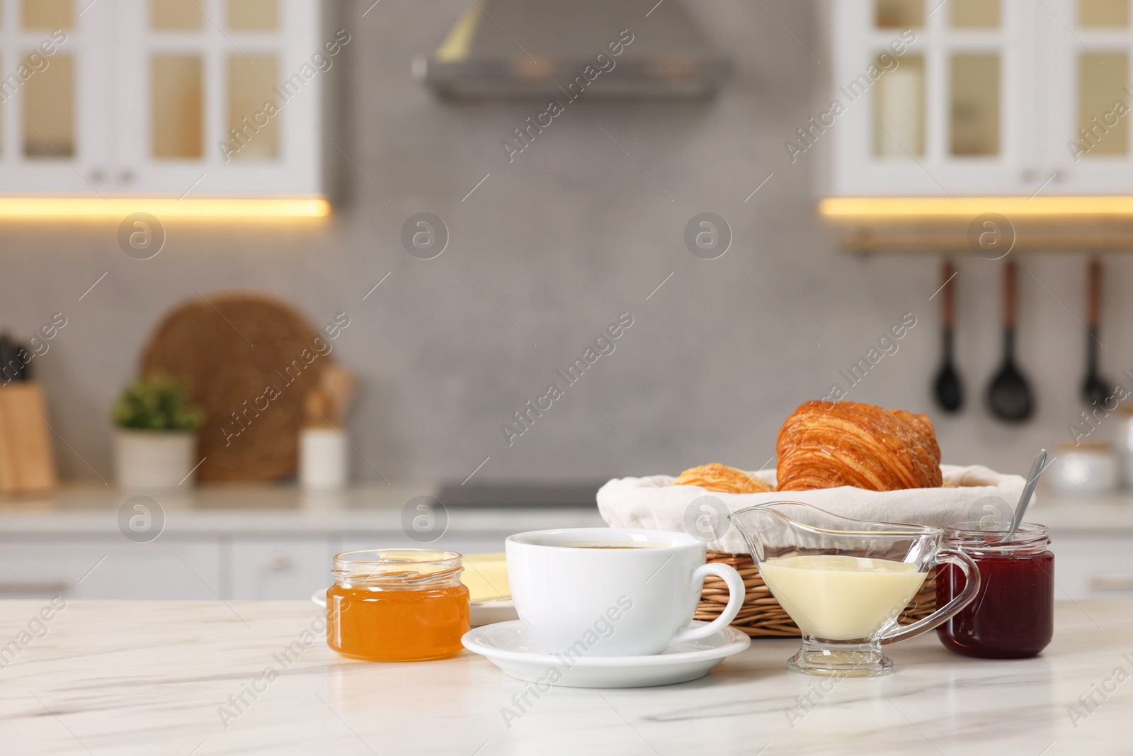 Photo of Breakfast served in kitchen. Fresh croissants, coffee, jam, honey and sweetened condensed milk on white table. Space for text