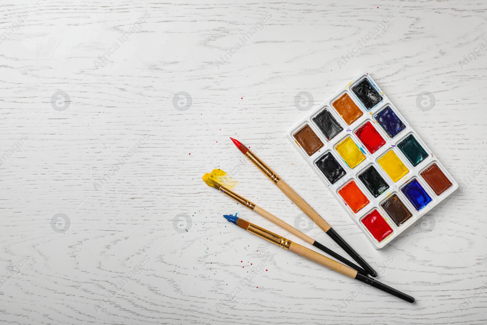 Photo of Plastic palette with colorful paints and brushes on wooden background, top view