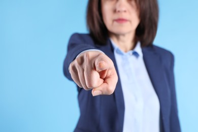 Woman in suit pointing with index finger on light blue background, closeup