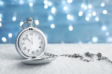 Photo of Pocket watch with snow on table against blurred lights. Christmas countdown