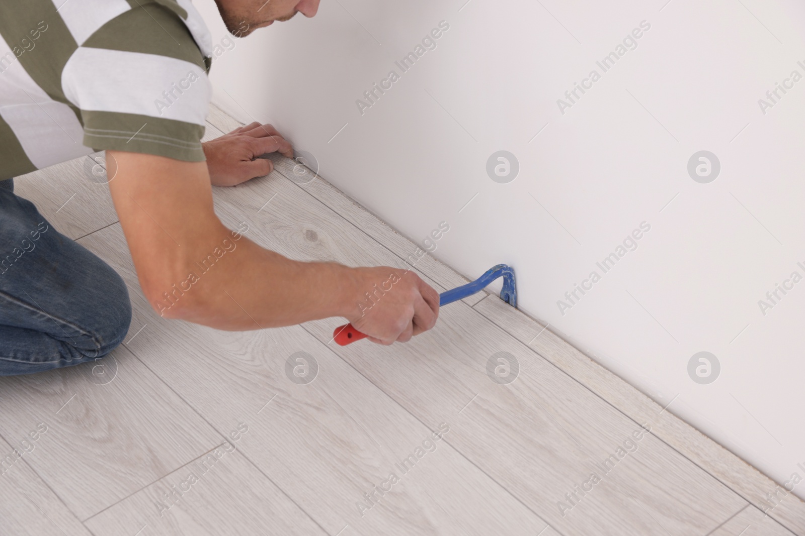 Photo of Professional worker using nail puller during installation of new laminate flooring indoors, closeup