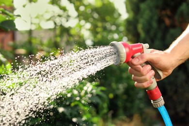 Man spraying water from hose in garden, closeup