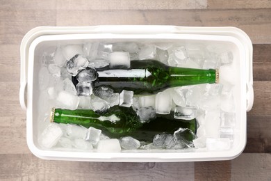Photo of Plastic cool box with ice cubes and beer on wooden floor, top view
