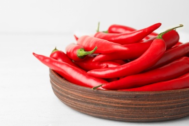 Wooden bowl with red hot chili peppers on white table, closeup