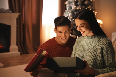 Couple opening gift box in living room with Christmas tree