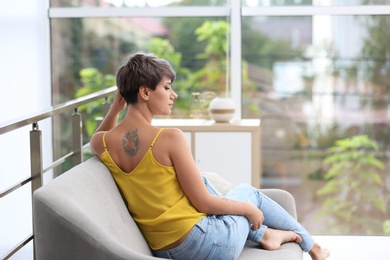 Trendy young woman with tattoo on sofa indoors