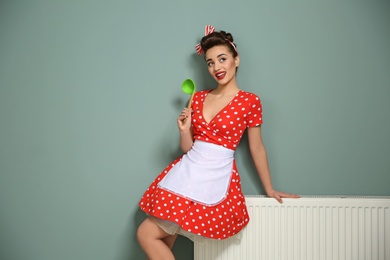 Funny young housewife with ladle near color wall