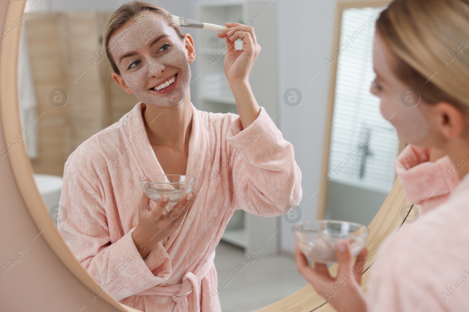 Photo of Woman applying face mask near mirror in bathroom. Spa treatments