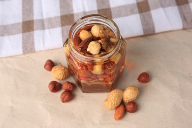 Jar with different nuts and honey on beige table