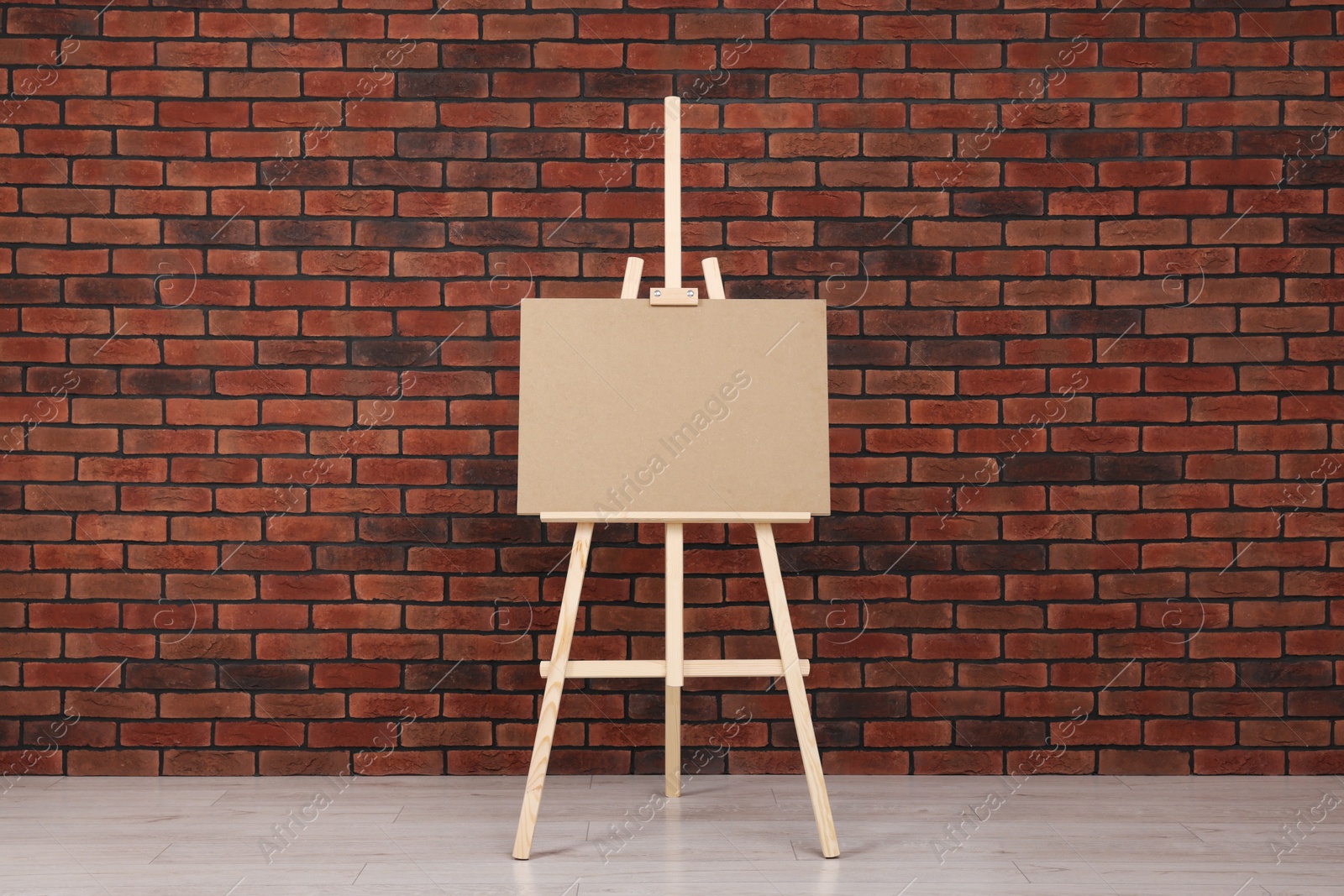 Photo of Wooden easel with blank board near brick wall indoors