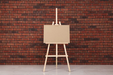 Photo of Wooden easel with blank board near brick wall indoors