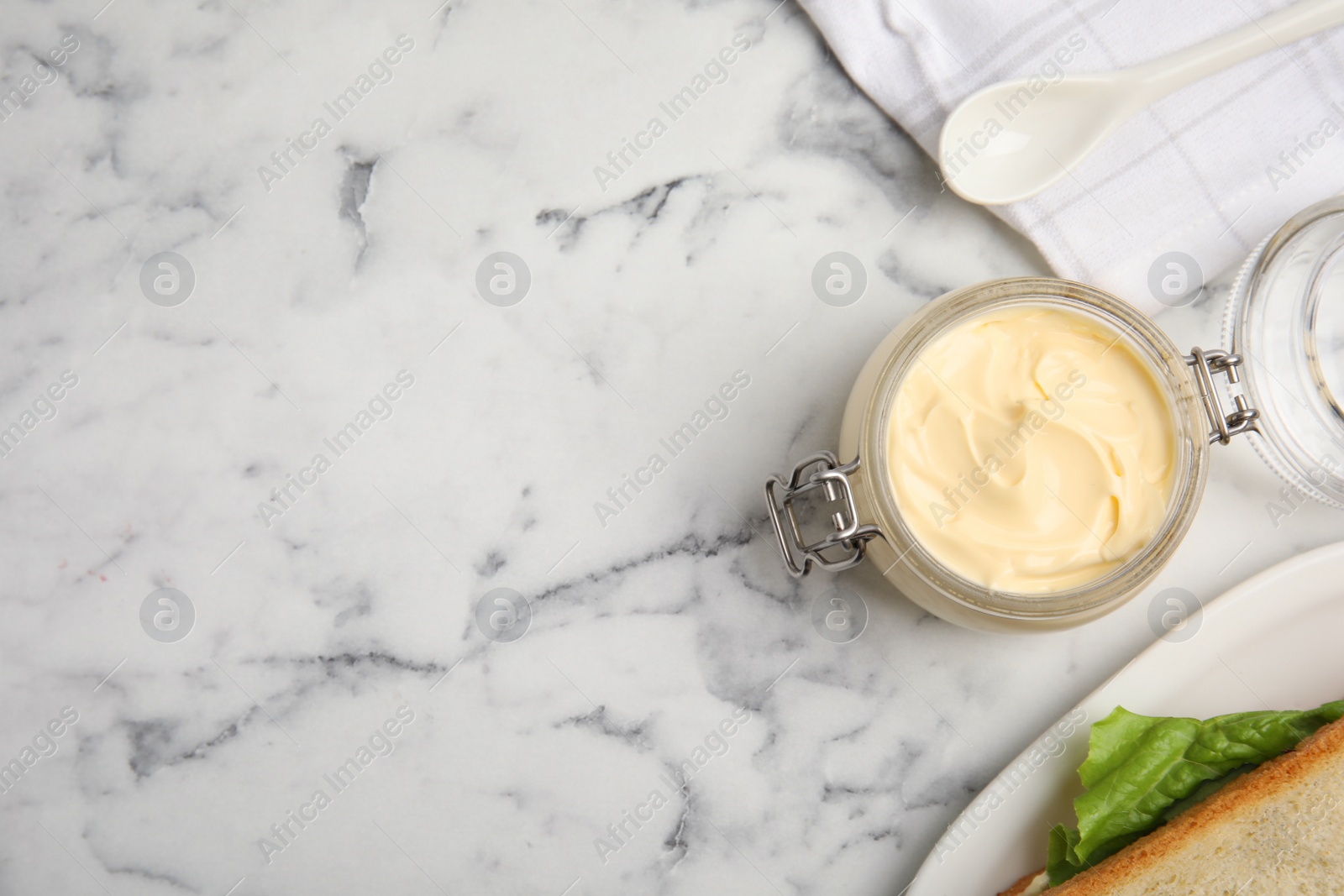 Photo of Jar of delicious mayonnaise near fresh sandwiches on white marble table, flat lay. Space for text