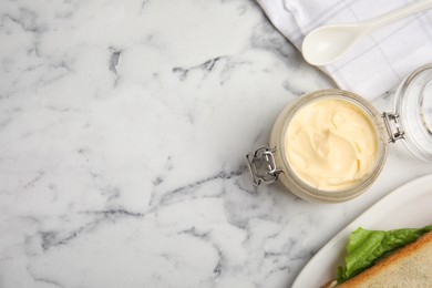 Photo of Jar of delicious mayonnaise near fresh sandwiches on white marble table, flat lay. Space for text