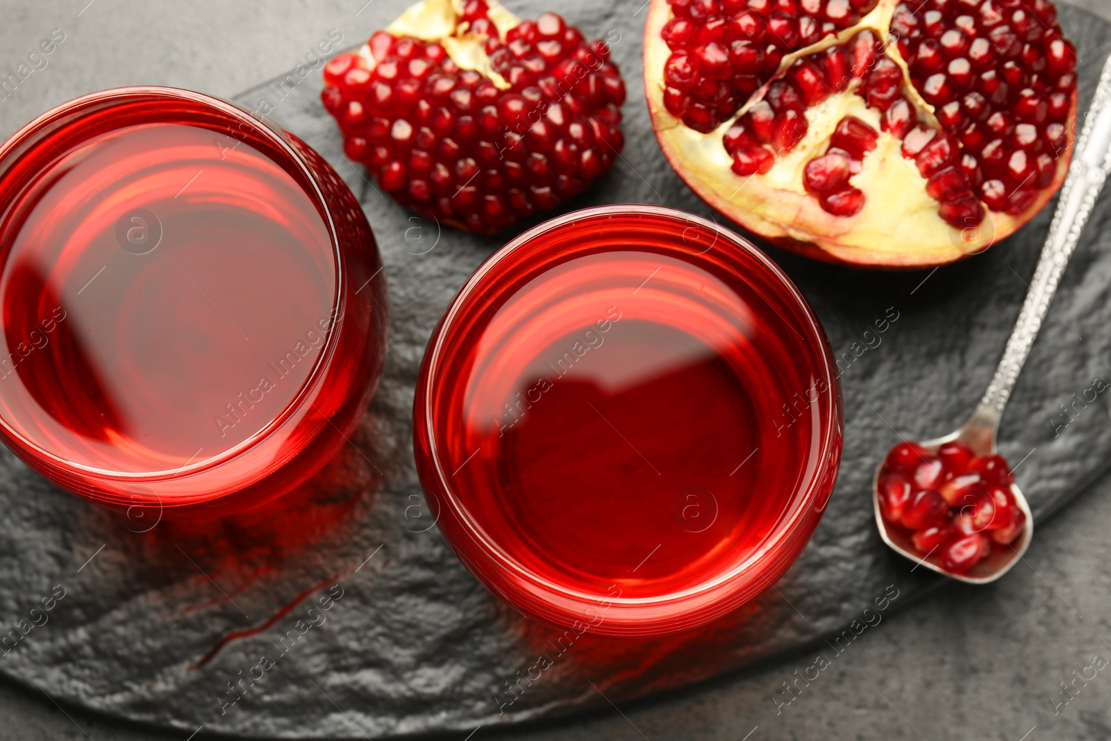 Photo of Tasty pomegranate juice in glasses and fresh fruit on grey table, top view