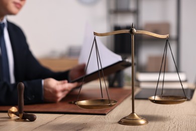 Photo of Notary working at wooden table in office, focus on scales of justice