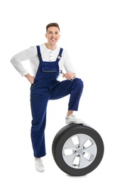 Male mechanic with car tire on white background