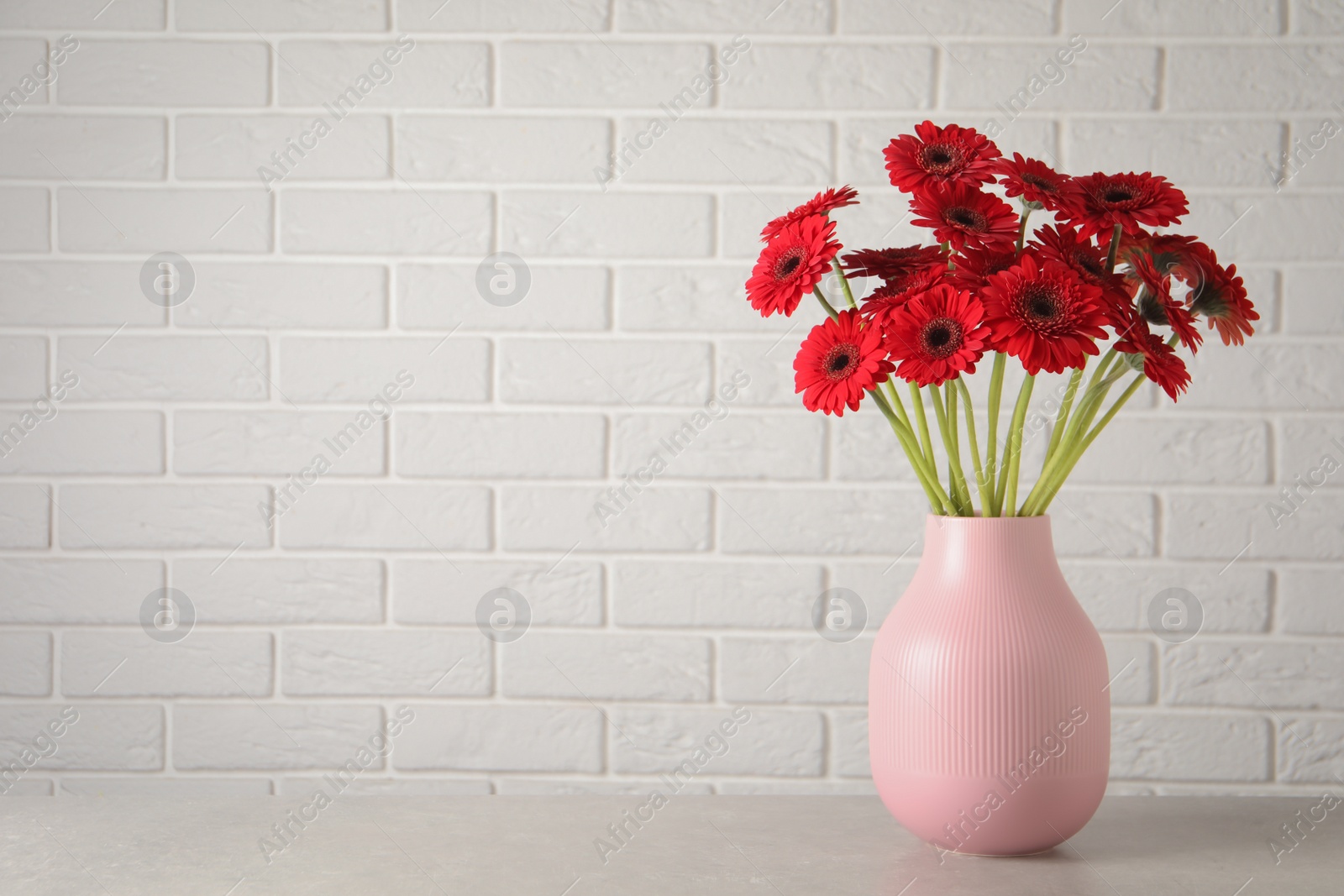 Photo of Bouquet of beautiful red gerbera flowers on table near white brick wall. Space for text