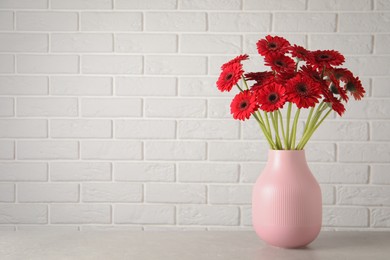 Bouquet of beautiful red gerbera flowers on table near white brick wall. Space for text