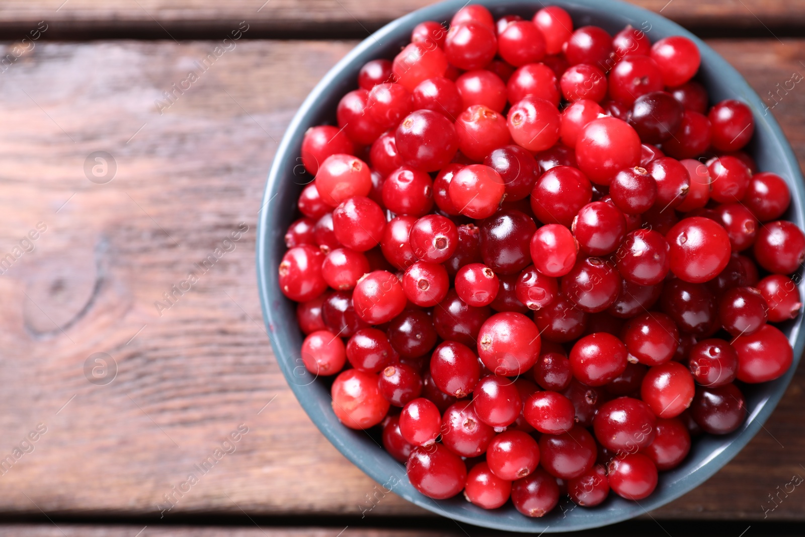 Photo of Fresh ripe cranberries in bowl on wooden table, top view