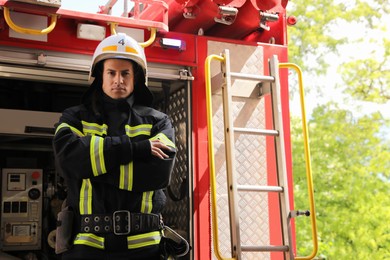 Photo of Portrait of firefighter in uniform and helmet near fire truck outdoors