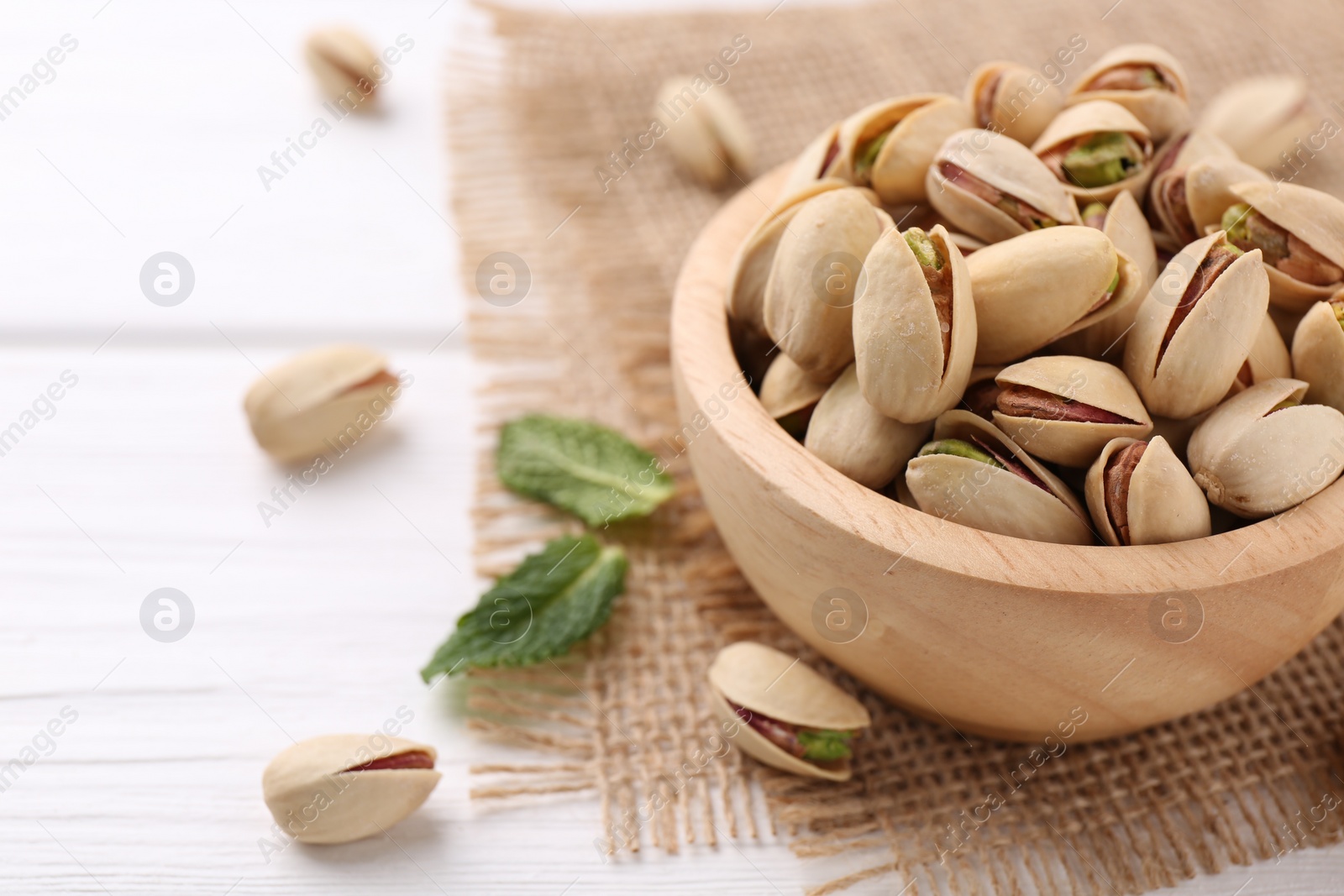 Photo of Tasty pistachios in bowl on white wooden table, closeup. Space for text
