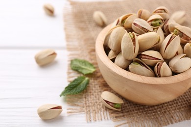 Tasty pistachios in bowl on white wooden table, closeup. Space for text