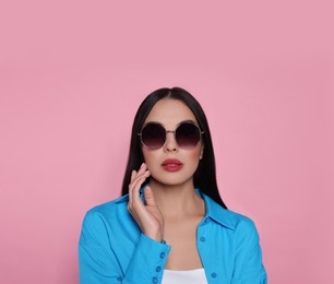 Photo of Attractive serious woman in fashionable sunglasses against pink background