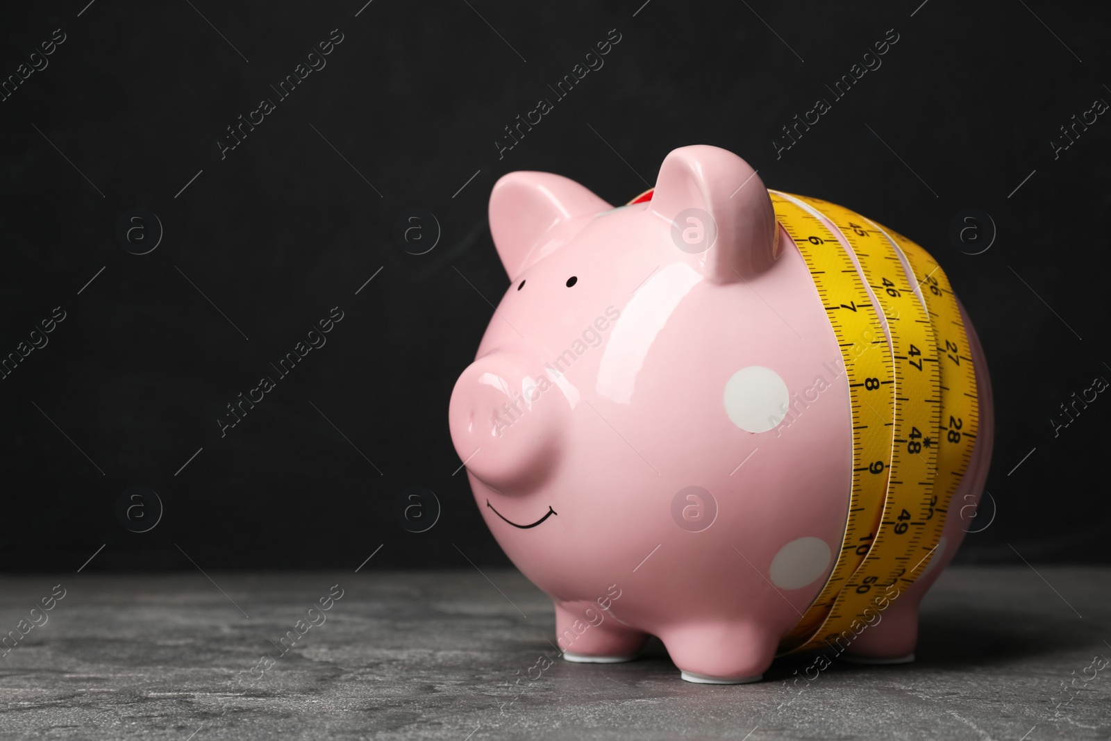 Photo of Piggy bank with measuring tape on table. Space for text