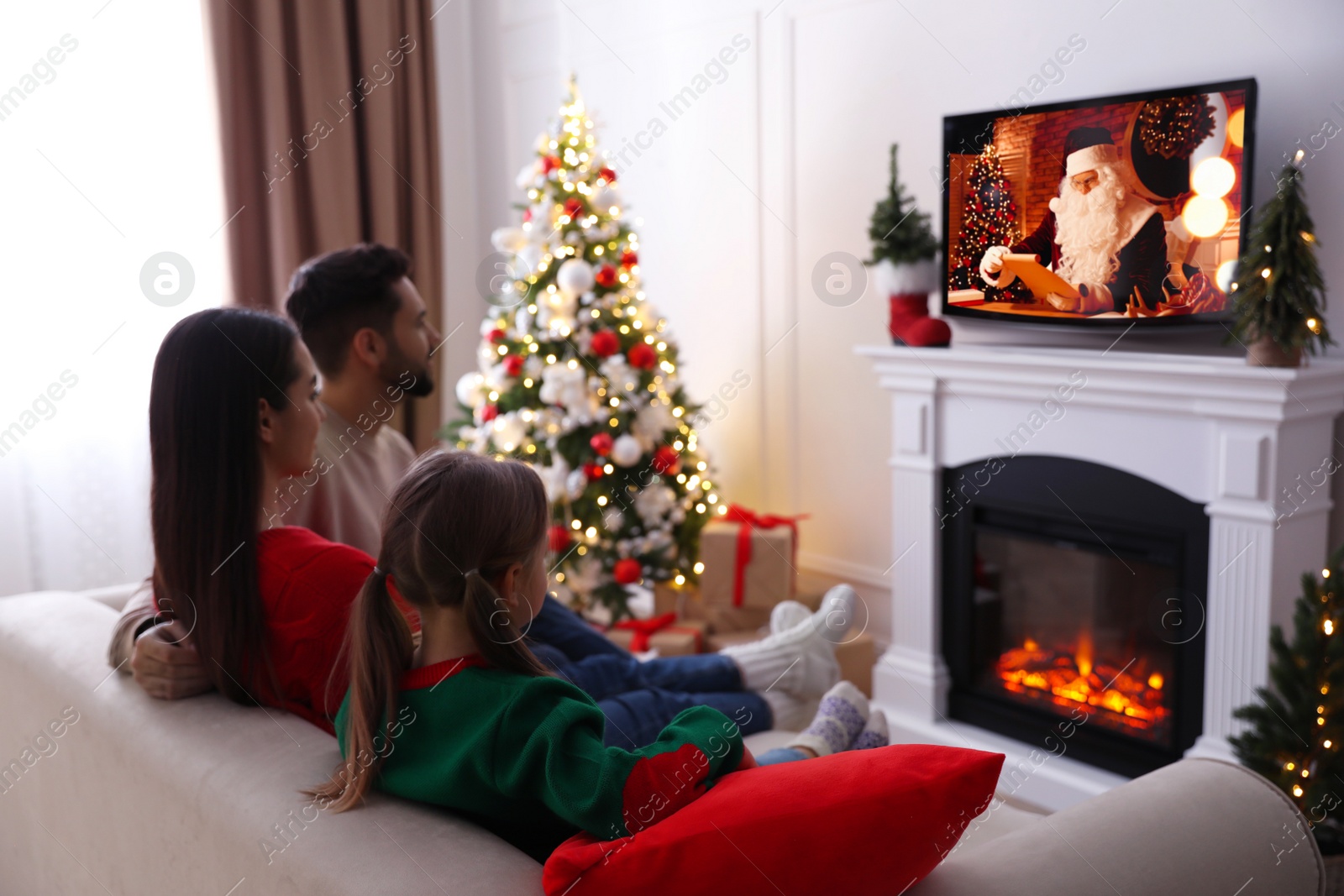 Image of Family watching festive movie on TV in room decorated for Christmas