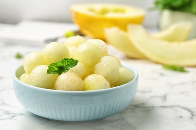 Photo of Plate of melon balls with mint on white marble table, closeup