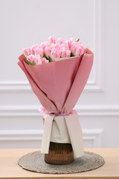 Beautiful bouquet of fresh pink tulips on wooden table near white wall