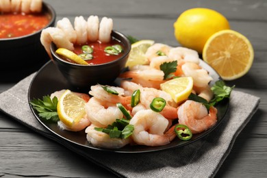 Photo of Tasty boiled shrimps with cocktail sauce, chili, parsley and lemon on grey wooden table