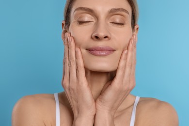 Photo of Woman massaging her face on turquoise background