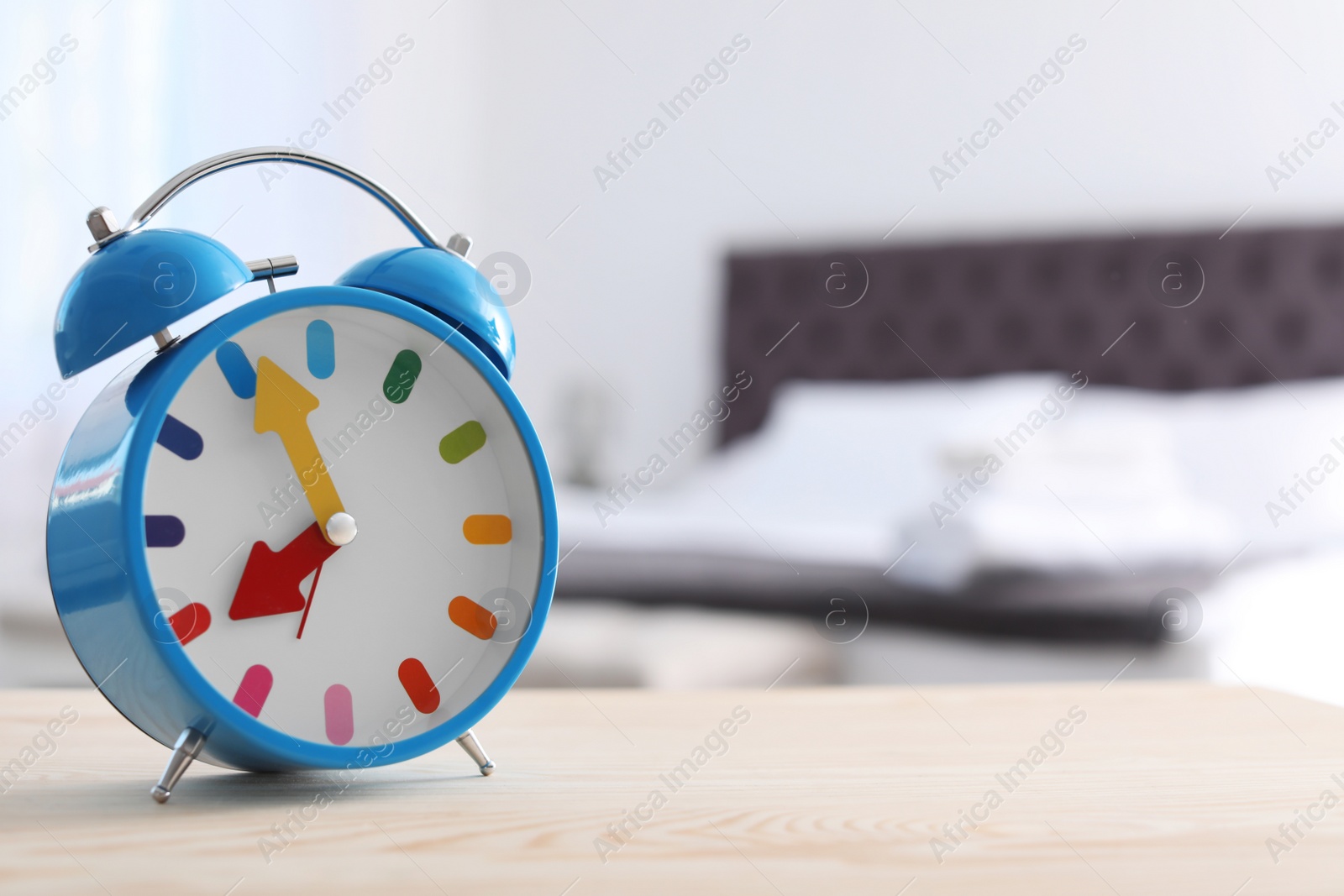 Photo of Colorful alarm clock on table in bedroom. Time to wake up