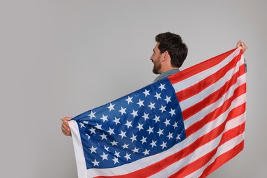 Photo of 4th of July - Independence Day of USA. Happy man with American flag on grey background, back view. Space for text