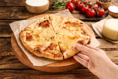 Photo of Woman taking piece of delicious khachapuri with cheese at wooden table, closeup