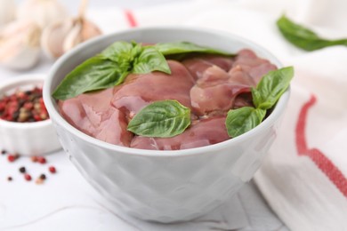 Bowl with raw chicken liver and basil on white textured table, closeup