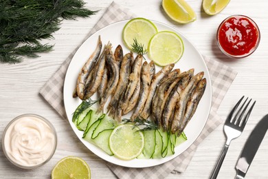 Photo of Delicious fried anchovies with lime, cucumber and sauces served on white wooden table, flat lay