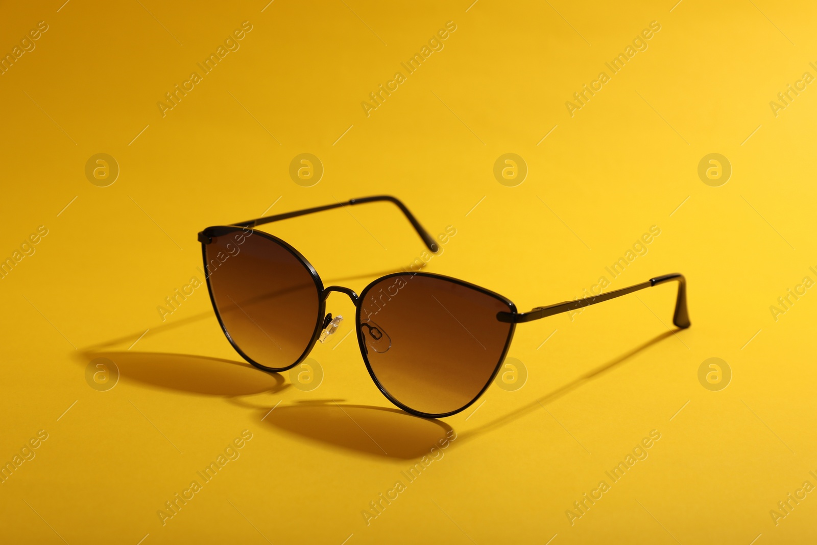 Photo of Stylish pair of sunglasses on yellow background