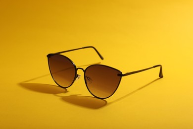 Photo of Stylish pair of sunglasses on yellow background