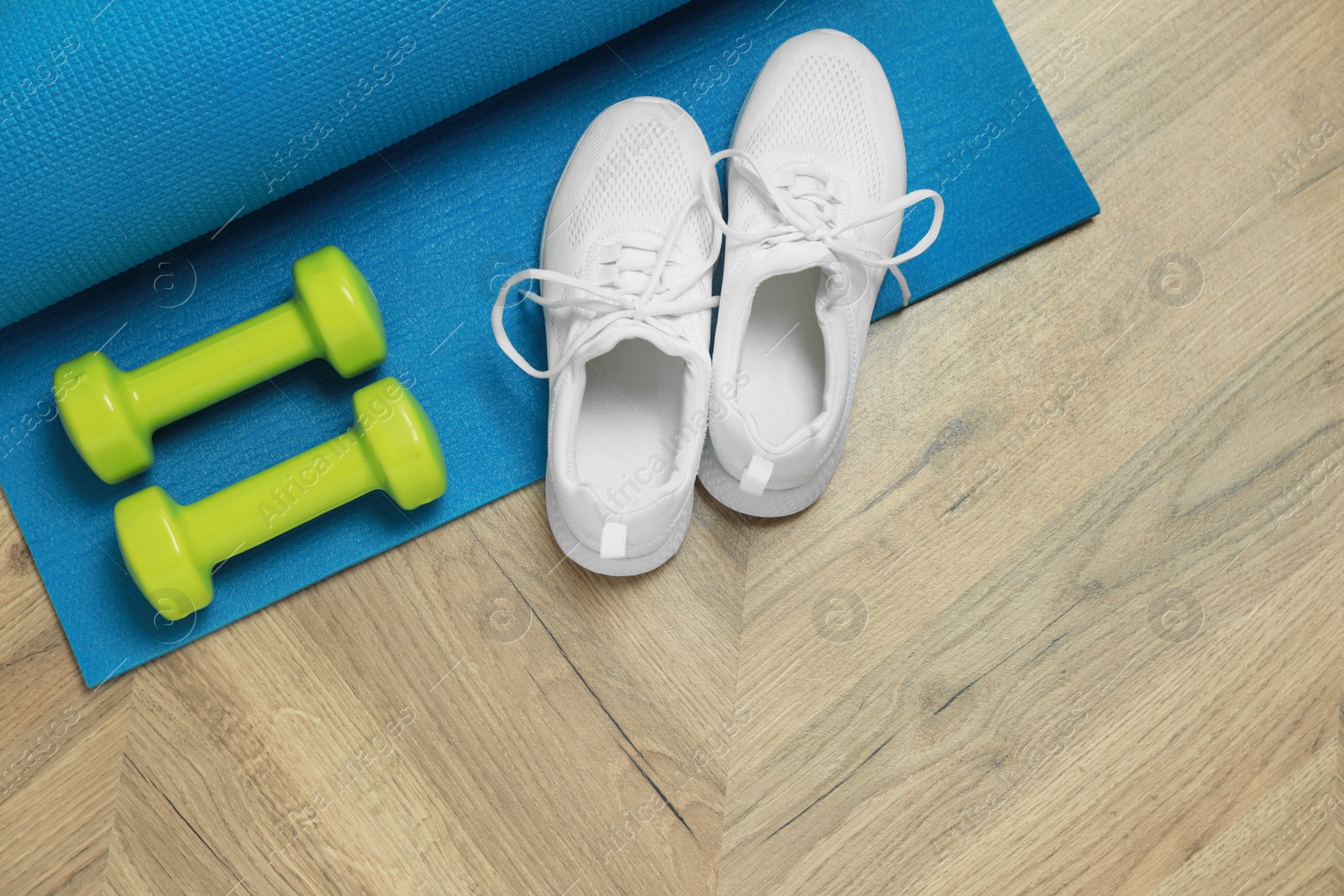 Photo of Dumbbells, sneakers and mat on wooden floor, top view. Space for text