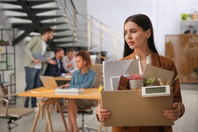 Upset dismissed young woman carrying box with stuff in office, space for text