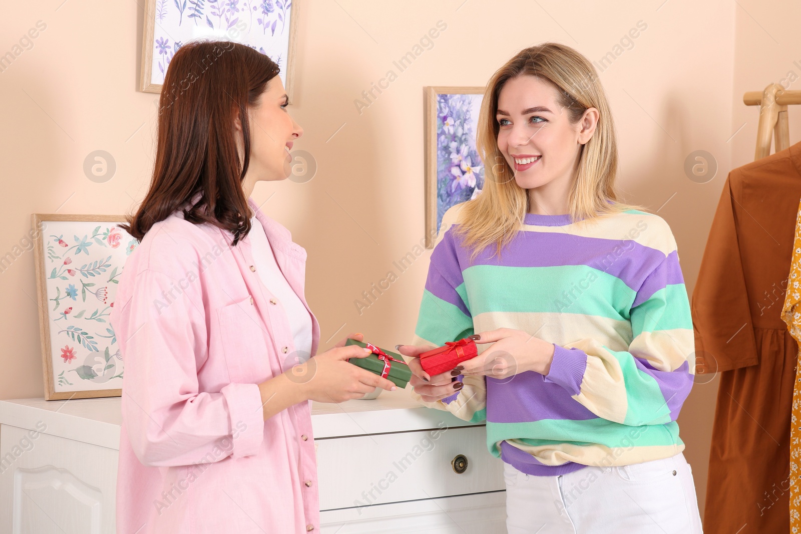 Photo of Smiling young women presenting gifts to each other indoors