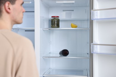 Photo of Upset man near empty refrigerator, selective focus
