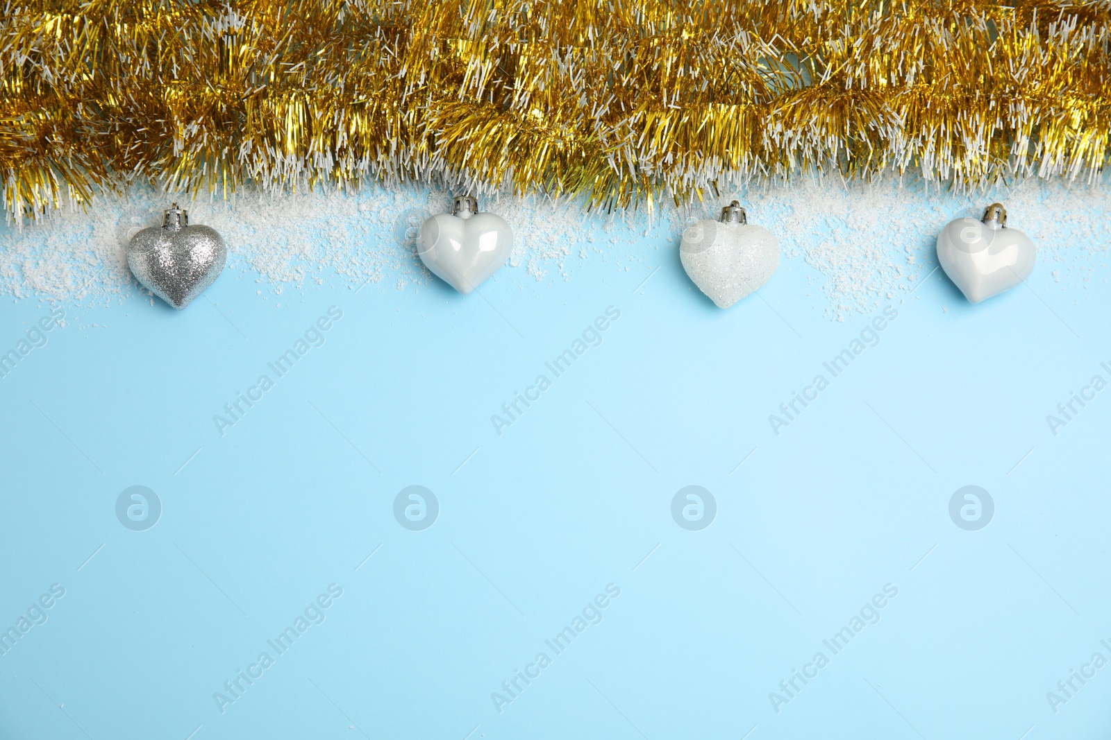 Photo of Shiny golden tinsel, Christmas baubles and snow on light blue background, flat lay. Space for text