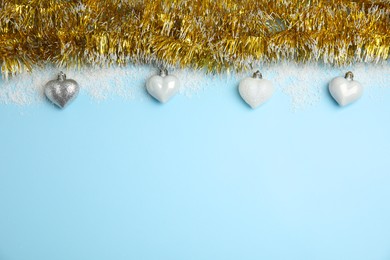 Photo of Shiny golden tinsel, Christmas baubles and snow on light blue background, flat lay. Space for text