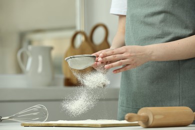 Woman sieving flour at table in kitchen, closeup. Space for text